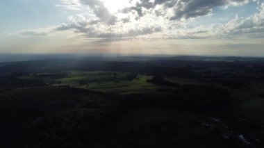 Altın güneş ışınları bulutları delip geçer, aşağıdaki yemyeşil kırları aydınlatır. Huzurlu manzara, alacakaranlıkta geniş gökyüzünün altında yuvarlanan tepeleri ve canlı yeşillikleri gösteriyor..