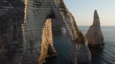 Güneş batarken, Etretat 'ın ünlü kayalıkları görkemli güzelliklerini gözler önüne seriyor. Yükselen kemerler ve kayalık oluşumlar ışıldayan sulara karşı tezat oluşturarak nefes kesici bir kıyı anı yaratıyor..