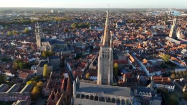 Bruges cazibesini gün batımında gösteriyor, Onze-Lieve-Vrouwekerk kulesini aydınlatıyor. Ortaçağ mimarisiyle süslenmiş bu tarihi şehrin güzelliğine tanık olun..