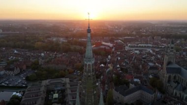 Güneş, Bruges 'ün siluetinin ardında batarken Onze-Lieve-Vrouwekerk' in muhteşem kulesi dimdik ayakta duruyor. Bu nefes kesici manzara şehrin alacakaranlıktaki cazibesini ve güzelliğini yansıtıyor..