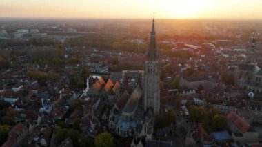 Güneş, Bruges 'deki Leydimizin tarihi kilisesinin arkasında batarken sıcak renkler çarpıcı mimariyi aydınlatıyor. Bu büyüleyici manzara, çevrenin zengin tarihini ve güzelliğini yansıtıyor..