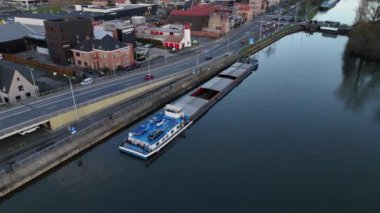 Bir mavna, nehir kenarındaki büyüleyici binalar tarafından çerçevelenmiş sakin sular boyunca sorunsuzca süzülür. Huzurlu atmosfer bu tuhaf yerin güzelliğini yansıtıyor, suda mükemmel bir gün sergiliyor..
