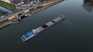 Sakin bir mavna, güzel bir manzarayla çevrili bir köprüye yaklaşırken sakin sularda süzülür. Öğleden sonra ışığı sahnede sıcak bir parıltı yayar ve güzelliğini arttırır..