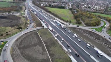 Yol çalışmaları sürerken yoğun trafik çift yönlü otoyolu doldurarak sürücüler için önemli gecikmelere yol açıyor. Manzara, yoğun güzergahı çevreleyen kentsel ve kırsal manzaranın bir karışımını gösteriyor..