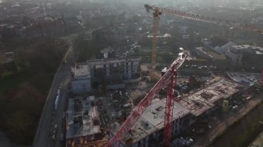 Gelişmekte olan bir şehir manzarasının üzerinde, bir inşaat alanının üzerinde vinç kulesi. İşçiler ve makineler işleriyle meşguller, binalar ortaya çıktıkça bölgenin büyümesine katkıda bulunuyorlar.