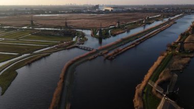 Alacakaranlık Kinderdijk 'in üzerine çökerken ikonik yel değirmenleri dingin sulara karşı dik dururlar. Manzara yumuşak renklerle parlıyor, tarih ve güzelliklerle dolu büyülü bir atmosfer yaratıyor..