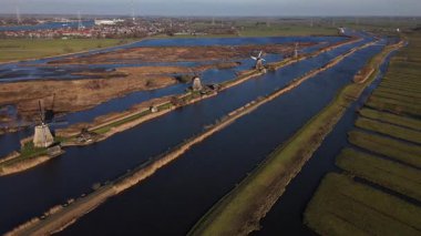 Kinderdijk 'in üzerine alacakaranlık çöktüğünde ikonik yel değirmenleri sönen ışığa karşı dik dururlar. Su yolları ve tarlalar boyunca sükuneti yansıtan sakin bir manzara ortaya çıkar..