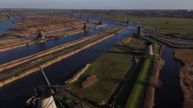 Güneş ufkun altına batarken, Kinderdijk yel değirmenleri durgun sulara yansıyan ve yemyeşil sularla çevrili canlı bir gökyüzüne karşı dimdik dururlar. Huzurlu bir akşam başlıyor.