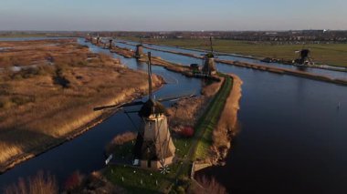 Güneş ikonik yel değirmenlerinin arkasında batarken Kinderdijk 'in dingin güzelliğini keşfedin. Gölgeler sakin sularda dans eder, Hollanda mirasının özünü büyülü bir alacakaranlık atmosferinde yakalar..