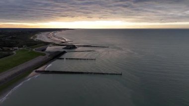 Hollanda 'nın sakin kıyı şeridini keşfedin. Gemiler ve yatlar alacakaranlıkta usulca suyun üzerinde süzülüyor. Gökyüzünün canlı renkleri dalgaları yansıtıyor ve sakin bir atmosfer yaratıyor..