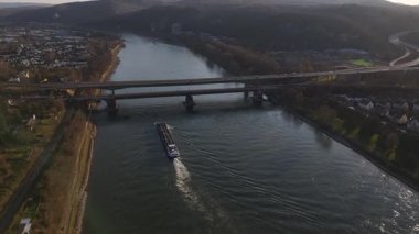 Güneş Koblenz 'ın üzerinde batarken sihirli renkler Ren Nehri' ni yansıtıyor. Manzaralı şehir silueti ufku aydınlatırken, bir mavna sularda sorunsuzca yol alır..
