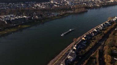 Güneş Koblenz üzerinde batarken Ren Nehri boyunca sakin bir mavna süzülür. Şehrin ufuk çizgisi suya yansıyarak, altın rengi ve dingin titreşimlerden oluşan görkemli bir panorama yaratıyor..
