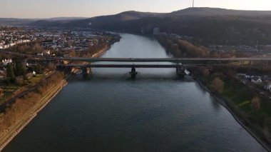 Güneş Koblenz üzerinde batarken köprü zarif bir şekilde Ren Nehri 'ni kaplar. Trenler raylar boyunca süzülürken, titreyen sular gün ışığını yansıtıyor ve sakin bir akşam atmosferi yaratıyor..