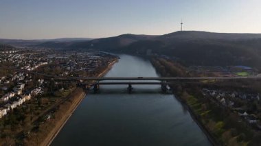 Koblenz 'de gece çökerken, Ren Nehri' nin sakin manzarasının tadını çıkarın, tek bir mavna pürüzsüz bir şekilde süzülerek, huzurlu manzarayı aydınlatacak, yumuşak parıltı ve huzur dolu hareketleriyle.