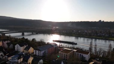 Güneş Koblenz 'in üzerinde batarken, sıcak parıltı gökyüzünü boyarken bir mavna zarif bir şekilde Ren Nehri boyunca yelken açarak bu güzel manzarada sakin bir an yaratıyor..