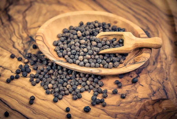 stock image many black peppercorns on olive wood