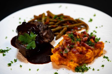 Tatlı patates püresiyle dana yanakları ve domates soslu fasulye ve sarımsaklı pastırma.