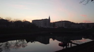 Motta di Livenza belediyesinin hava görüntüsü, insansız hava aracı, çan kulesi olan saraylar ve kiliseler, gün batımında nehir kıyısında.