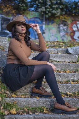 Kahverengi şapkalı ve sonbahar yapraklı merdivenlerde oturan düşünceli kadın..