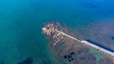 Sakin deniz dalgaları, kayalar ve kristal berrak zümrüt suyuyla insansız hava aracı manzarası. Altın plajın ortasındaki insanlar için köprü.