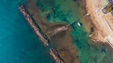 Sakin deniz dalgaları, kayalar ve kristal berrak zümrüt suyuyla insansız hava aracı manzarası. Altın plajın ortasındaki insanlar için köprü.