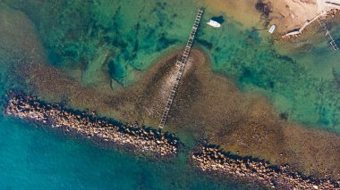 Sakin deniz dalgaları, kayalar ve kristal berrak zümrüt suyuyla insansız hava aracı manzarası. Altın plajın ortasındaki insanlar için köprü.
