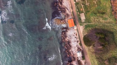 Köpüklü deniz dalgalarının drone çekimi altın renkli kıyılara çarpıyor dalgalı ve rüzgarlı dalgalı deniz. Kahverengi kayalar. 4K videolar, kırmızı ev