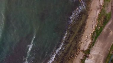 Köpüklü deniz dalgalarının drone çekimi altın renkli kıyılara çarpıyor dalgalı ve rüzgarlı dalgalı deniz. Kahverengi kayalar. 4K videoları