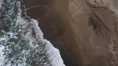 Köpüklü deniz dalgalarının drone çekimi altın renkli kıyılara çarpıyor dalgalı ve rüzgarlı dalgalı deniz. kayalar