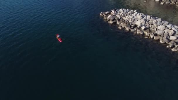 海でスポーツをしている2人の上からのビデオ 赤いカヌーで クリスタルクリア海 岩や砂と背景 — ストック動画
