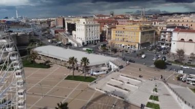 Civitavecchia şehrinin panoramik manzarası ve bitişik turizm limanı ve Forte Michelangelo. Tropik palmiye ağaçlarıyla zümrüt deniz ve manzara. Dönme dolap ve bulutlu gökyüzü.