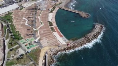 Panoramic view of the city of Civitavecchia with the adjoining tourist port and Forte Michelangelo. Emerald sea and view with tropical palm trees. Ferris wheel and cloudy sky.