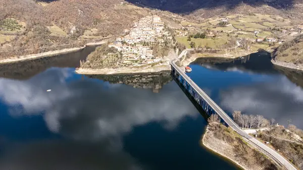 Turano Gölü 'nün panoramik hava manzarası. Zümrüt suyuyla göl, tünemiş kasabayla kış manzarası. Suyun üzerindeki köprüye bağlanıyor