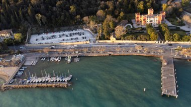Garda şehrinin insansız hava aracı ile hava görüntüsü. Göl kıyısında aynı isimde bir kasaba, gün batımında mavi deniz, uzakta martılar ve tekneler..