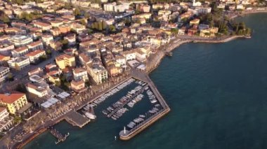 Garda şehrinin insansız hava aracı ile hava görüntüsü. Göl kıyısında aynı isimde bir kasaba, gün batımında mavi deniz, uzakta martılar ve tekneler..