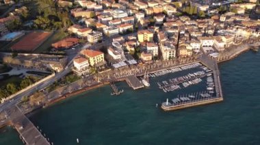Garda şehrinin insansız hava aracı ile hava görüntüsü. Göl kıyısında aynı isimde bir kasaba, gün batımında mavi deniz, uzakta martılar ve tekneler..
