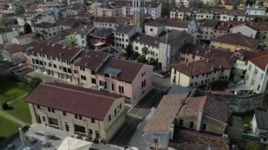 Küçük bir İtalyan kasabasının hava görüntüsü. Veneto, Treviso vilayetindeki Motta di livenza. Nehrin kıyısındaki köprü, karakteristik kırmızı evler, nehir kenarındaki ağaçlar. Bahar ilerliyor. Kilise çanı çalıyor..