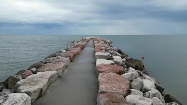 Plajlı ve kurşuni kayalıklı pürüzsüz deniz. Baharın sonları, bulutlu gökyüzü ve yaklaşan yağmur. İtalya, Veneto, Eraclea kıyısı