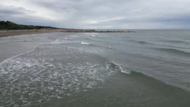 Plajlı ve kurşuni kayalıklı pürüzsüz deniz. Baharın sonları, bulutlu gökyüzü ve yaklaşan yağmur. İtalya, Veneto, Eraclea kıyısı