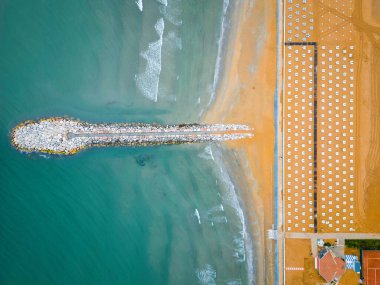 Plajlı ve kurşuni kayalıklı pürüzsüz deniz. Baharın sonları, bulutlu gökyüzü ve yaklaşan yağmur. İtalya, Veneto, Eraclea kıyıları. Güneş.