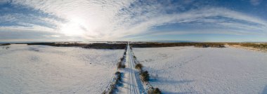 Uzakta kaybolan ve karlı tarlalarla çevrili karla kaplı bir kır yolu boyunca hava manzarası.