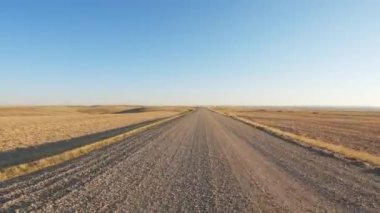 Sonbaharda, çakıllı bir yolda, açık çayırlardan geçen bir aracın ön tarafındaki POV. Kamyon Teksas sığır geçidini geçmek için yavaşlıyor. Gökyüzü puslu beyaz bulutlarla mavidir.