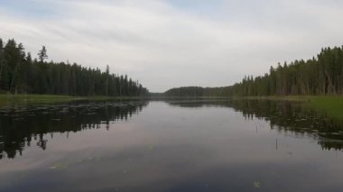 Bir kanonun ön tarafına monte edilmiş kamera sazlıklar arasında yavaşça hareket ediyor ve sonra da nilüfer yaprağıyla sakin bir göl boyunca ilerliyor. Göl sık ve yeşil bir ormanla çevrilidir..