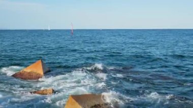 Gün batımında Balear Denizi 'ndeki Dalgakıranlara Karşı Su Sıçramaları' nın Yakın Çekimi. Barcelona, İspanya 'daki Pier On Beach' ten görüntü. Horizon 'da yelkenli gemiler. Yüksek kalite 4k görüntü