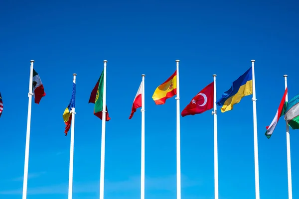 Flags of Different Countries Hang On Flagpoles Against Blue Sky. Flag of Spain, Ukraine, Mexico, Germany, Sweden, Turkey and Poland. The concept of support and unity of countries. High quality photo