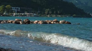 Pebble Plajı, Taş İskele ve İyon Denizi Dalgaları, Moraitika, Korfu, Yunanistan. Otel ve Yürüyen Tatilciler Arkaplanda. Yüksek kalite 4k görüntü