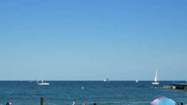 Barcelona, İspanya - 05: 29 2022: İnsanlar dinleniyor, güneşleniyor ve iskelede balık tutuyor, arka planda yelkenli tekneleri ve Horizon 'da kargo gemisi, Balear Denizi. Yüksek kalite 4k görüntü