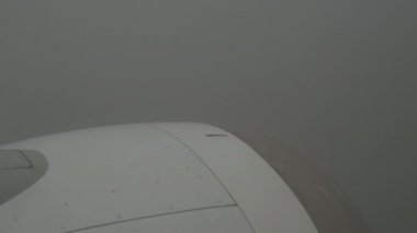 View from Airplane On Thick Gray Clouds, Sky Is Not Visible. Turbulence in bad weather. Through Clouds You Can See Forest And Houses. In frame White-Grey Engine Casing With Vanes. High quality 4k