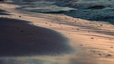 Kumlu plaj batan güneşin ışınlarında köpüklü deniz dalgalarıyla yıkanır. Su gözlemi ve rahatlama konsepti. Yüksek kalite 4k görüntü