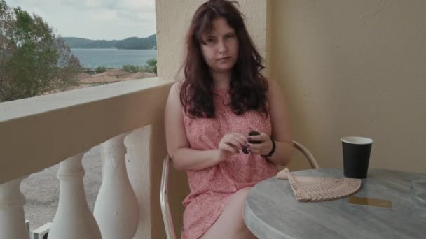 Młoda Kobieta Jasnej Sukience Siedzi Krześle Balkonie Hotelu Wkłada Słuchawkę — Wideo stockowe